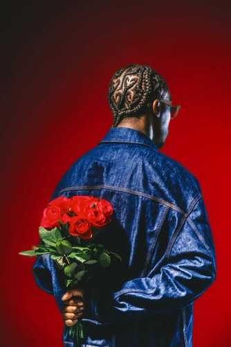 Model in a denim jacket seen from behind, holding red roses, against a red studio backdrop