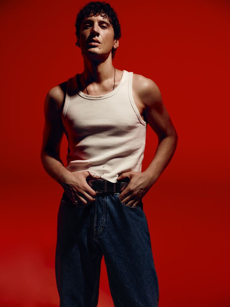 Model in a white tank and dark indigo jeans against a red studio backdrop
